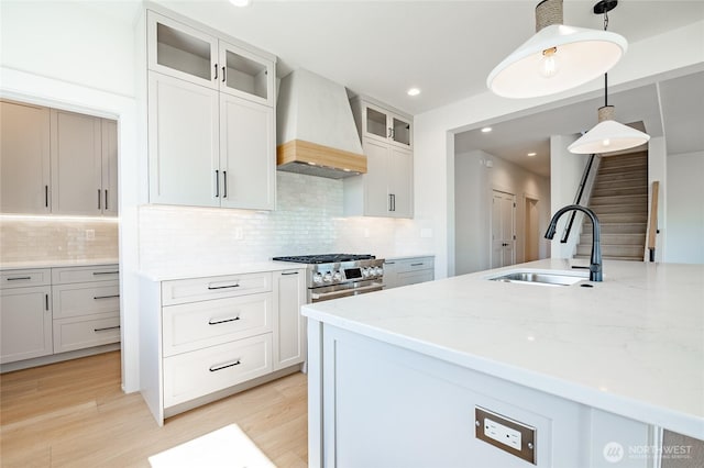 kitchen with pendant lighting, stainless steel range, a sink, light stone counters, and custom range hood