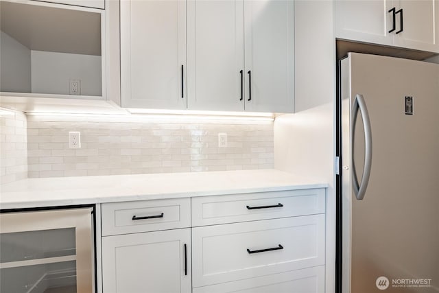 kitchen featuring beverage cooler, light stone counters, decorative backsplash, freestanding refrigerator, and white cabinets