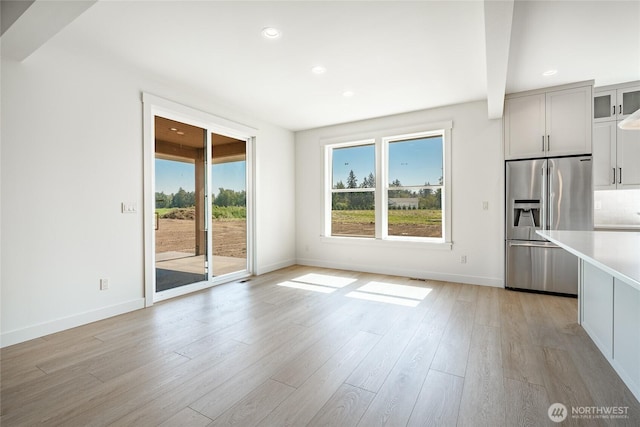 interior space featuring a wealth of natural light, backsplash, light wood finished floors, and stainless steel refrigerator with ice dispenser