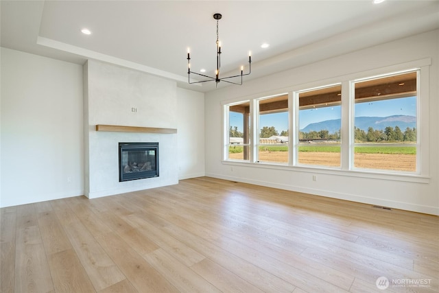 unfurnished living room with a glass covered fireplace, light wood-style floors, baseboards, and a chandelier