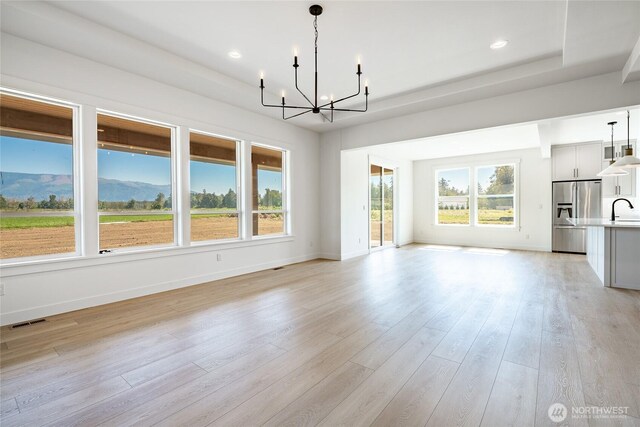 unfurnished living room featuring baseboards, visible vents, light wood-style flooring, a sink, and a notable chandelier