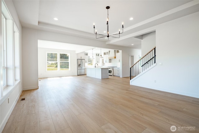 unfurnished living room featuring visible vents, a sink, stairway, light wood-style floors, and a chandelier