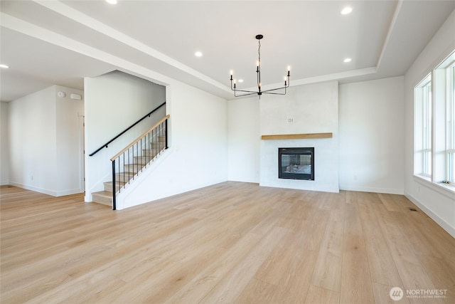 unfurnished living room featuring a tray ceiling, a glass covered fireplace, wood finished floors, recessed lighting, and stairway