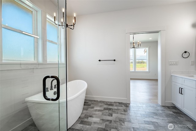 bathroom featuring a freestanding tub, baseboards, a notable chandelier, and vanity