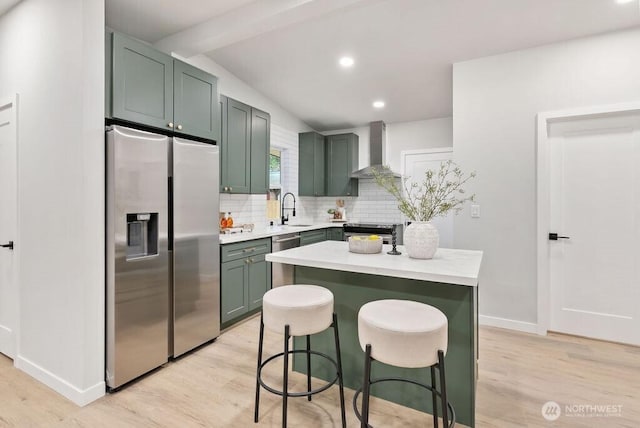 kitchen with a sink, appliances with stainless steel finishes, green cabinets, wall chimney range hood, and decorative backsplash