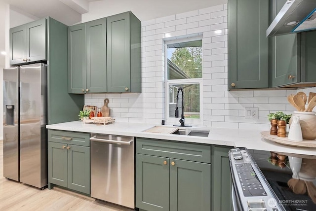 kitchen with a sink, light countertops, under cabinet range hood, appliances with stainless steel finishes, and green cabinets