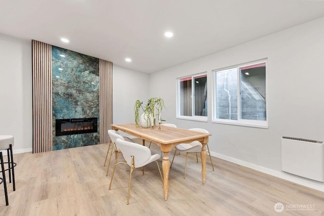 dining area featuring baseboards, a large fireplace, wood finished floors, and radiator heating unit