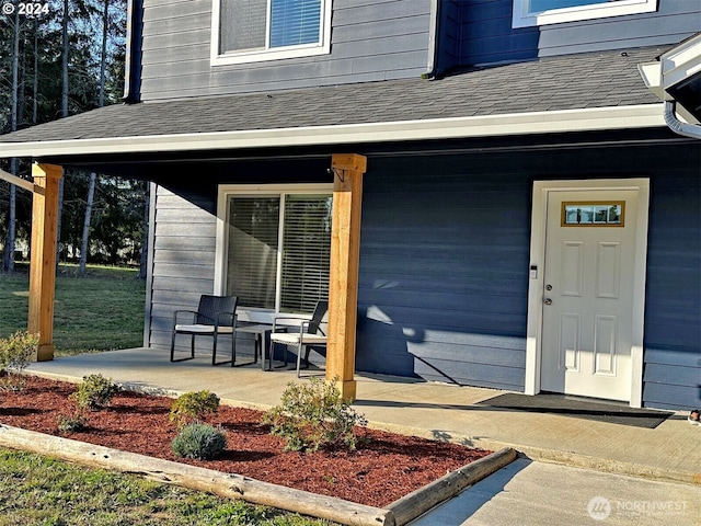 entrance to property with a porch and a shingled roof