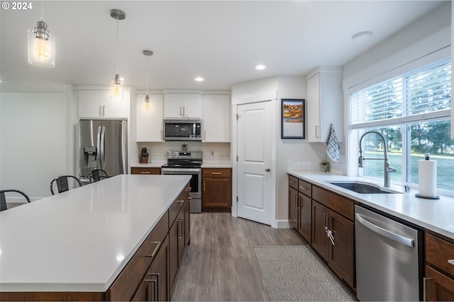 kitchen with a sink, decorative light fixtures, light wood-style floors, appliances with stainless steel finishes, and light countertops