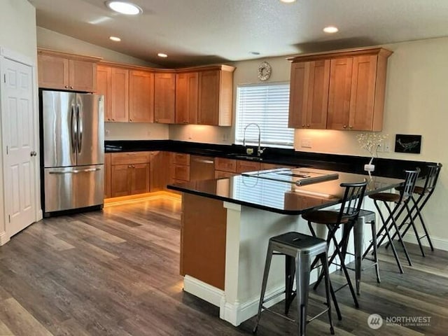 kitchen with a kitchen bar, a sink, dark wood-style floors, appliances with stainless steel finishes, and a peninsula