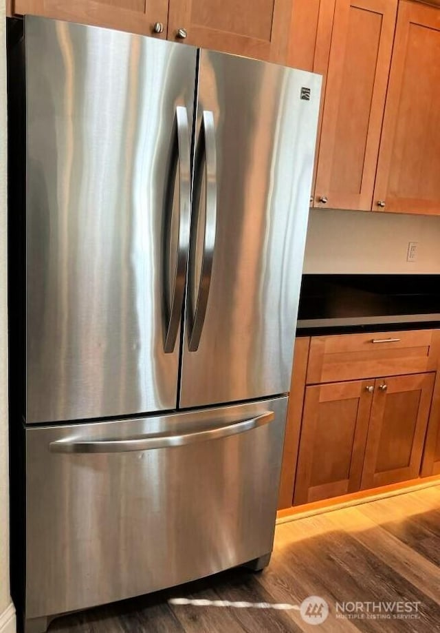 kitchen featuring dark countertops, wood finished floors, brown cabinetry, and freestanding refrigerator