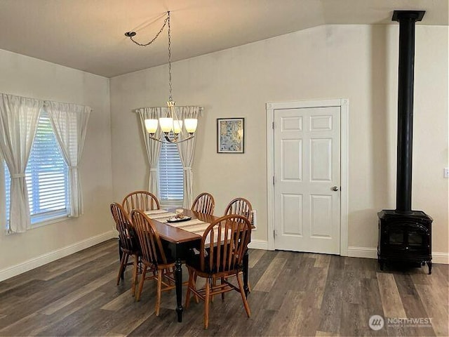 dining room with dark wood-type flooring, lofted ceiling, baseboards, a chandelier, and a wood stove