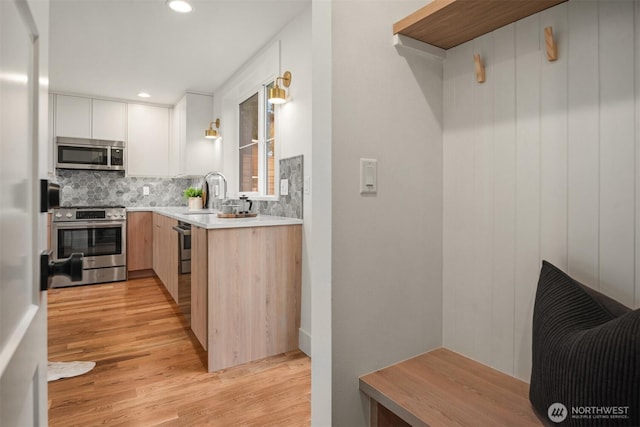 kitchen featuring decorative backsplash, stainless steel appliances, light wood-style floors, and a sink