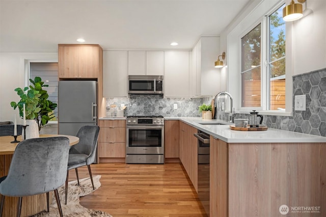 kitchen featuring a sink, stainless steel appliances, light countertops, light wood-type flooring, and backsplash