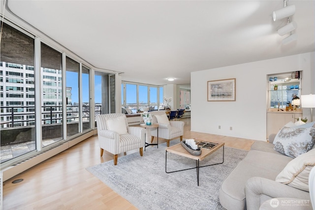 living area with a city view, floor to ceiling windows, wood finished floors, and a healthy amount of sunlight