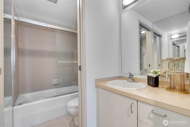 full bath featuring combined bath / shower with glass door, toilet, vanity, and tile patterned flooring