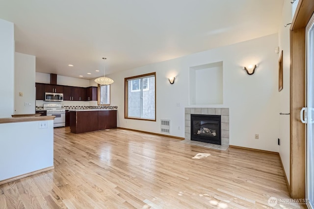 kitchen featuring stainless steel microwave, dark brown cabinets, open floor plan, white range with gas stovetop, and light wood-style floors