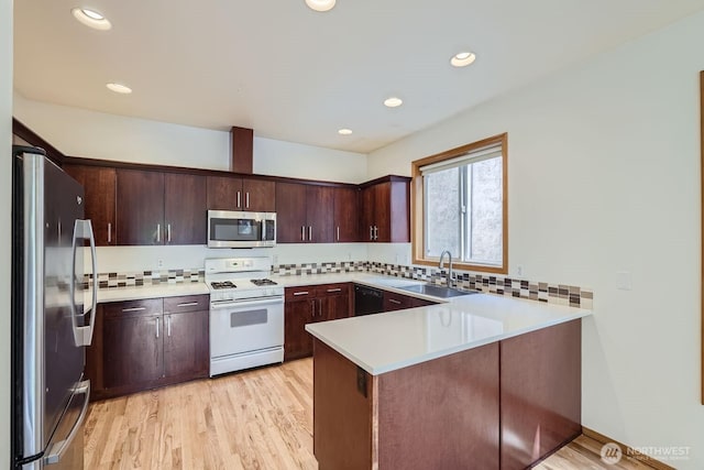 kitchen with appliances with stainless steel finishes, light wood-type flooring, a peninsula, and a sink