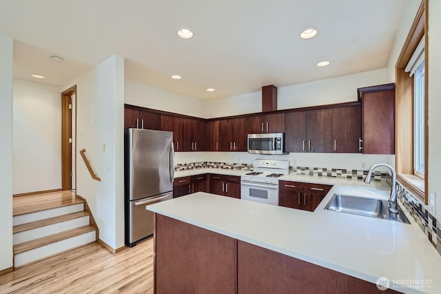 kitchen with a sink, stainless steel appliances, a peninsula, light countertops, and dark brown cabinets