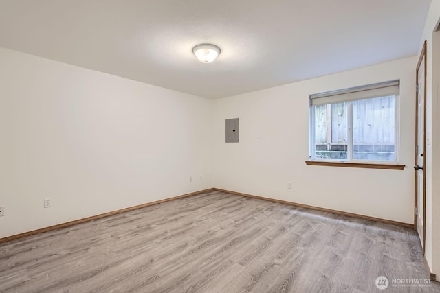 empty room with light wood finished floors, electric panel, and baseboards