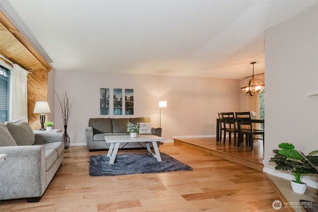 living area with an inviting chandelier, plenty of natural light, light wood-style floors, and baseboards