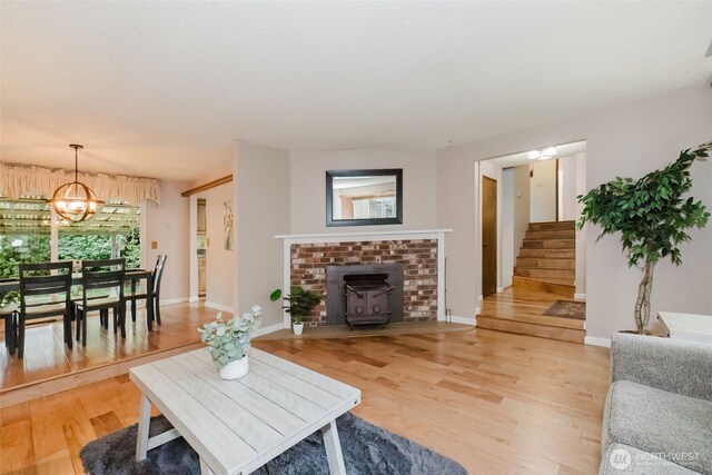 living area with an inviting chandelier, light wood-type flooring, stairs, and a wood stove