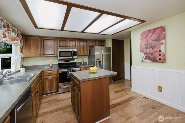 kitchen with light wood-type flooring, stainless steel appliances, a wainscoted wall, and a sink