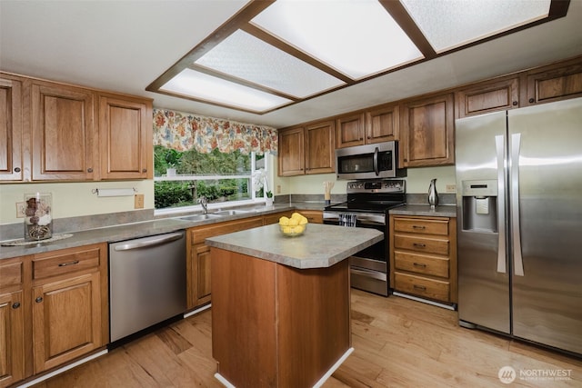 kitchen with brown cabinetry, stainless steel appliances, light wood-style floors, and a sink