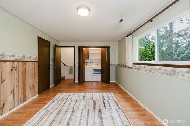 hall featuring washer and dryer, visible vents, a textured ceiling, and light wood finished floors