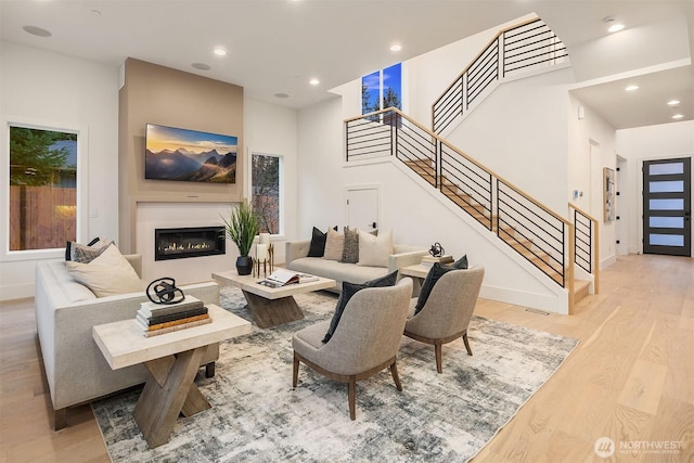 living area with recessed lighting, light wood-style floors, a glass covered fireplace, and stairs