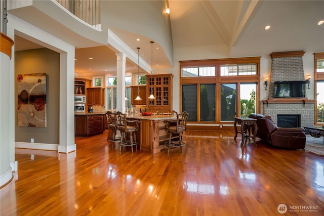 interior space with a kitchen breakfast bar, open floor plan, decorative columns, built in microwave, and a brick fireplace