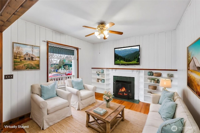 living room featuring a ceiling fan, a lit fireplace, and wood finished floors