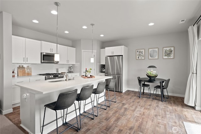 kitchen with a kitchen breakfast bar, an island with sink, wood finished floors, and stainless steel appliances