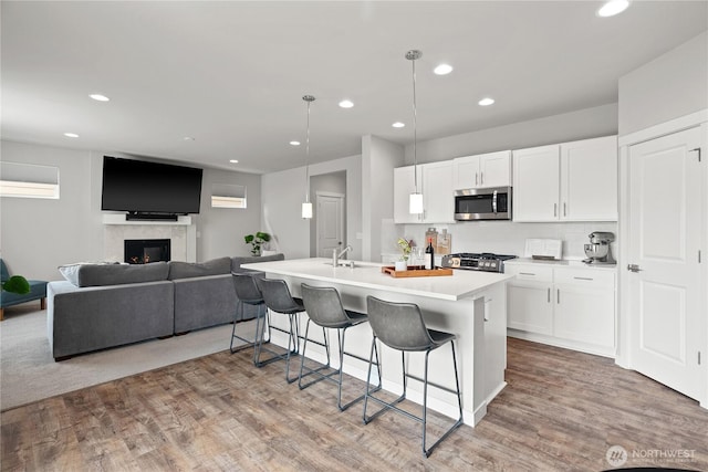 kitchen with a breakfast bar, stainless steel microwave, white cabinets, and a warm lit fireplace