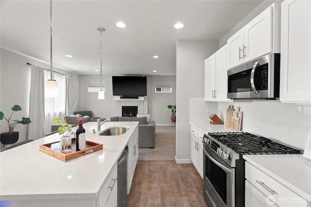 kitchen featuring backsplash, open floor plan, an island with sink, stainless steel appliances, and a sink