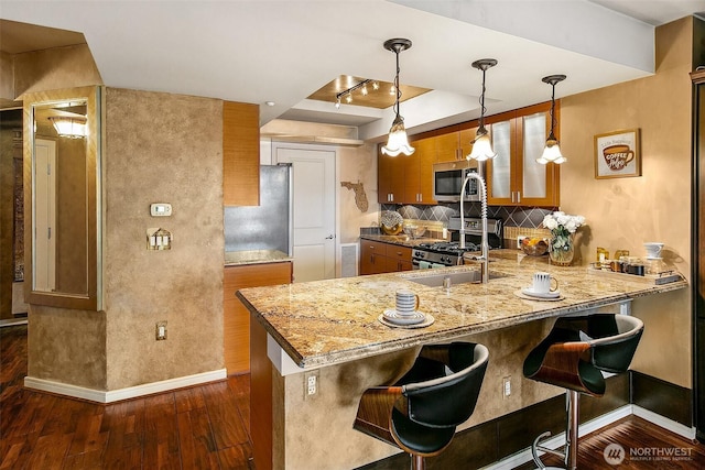 kitchen featuring tasteful backsplash, brown cabinets, appliances with stainless steel finishes, a peninsula, and dark wood-style floors