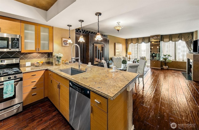 kitchen featuring dark wood-style floors, a peninsula, a sink, stainless steel appliances, and tasteful backsplash