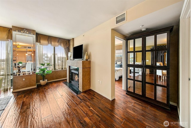 living room featuring a glass covered fireplace, baseboards, visible vents, and hardwood / wood-style floors