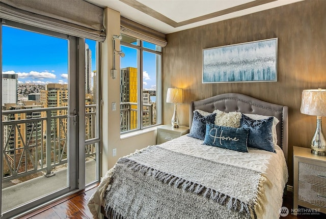 bedroom with a view of city, access to outside, and wood finished floors