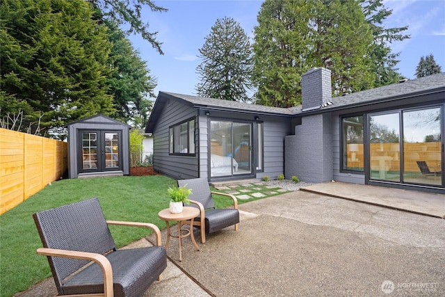 rear view of house featuring fence, a lawn, a chimney, an outdoor structure, and a patio