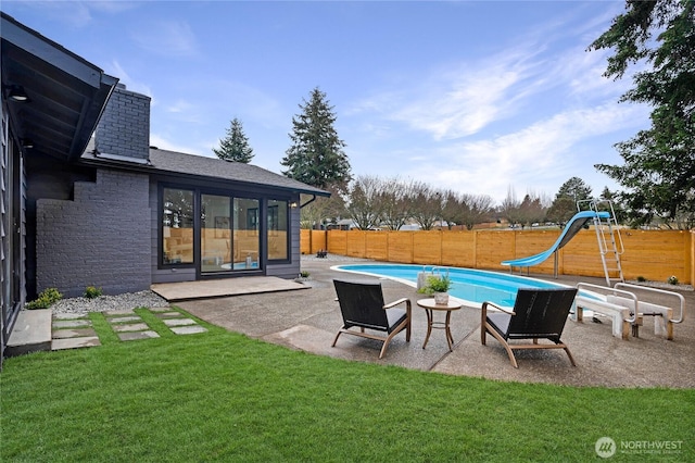 view of swimming pool featuring a lawn, a fenced backyard, a water slide, a fenced in pool, and a patio area