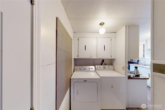 laundry room with washing machine and clothes dryer, cabinet space, and a textured ceiling