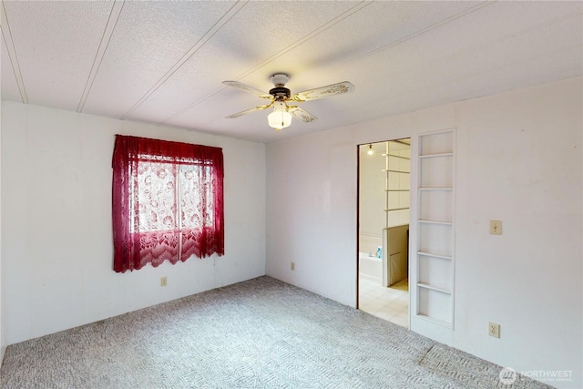 unfurnished bedroom with ceiling fan, light carpet, a textured ceiling, and ensuite bath