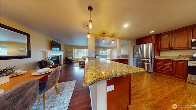 kitchen with light stone countertops, a tiled fireplace, pendant lighting, dark wood-style floors, and stainless steel appliances