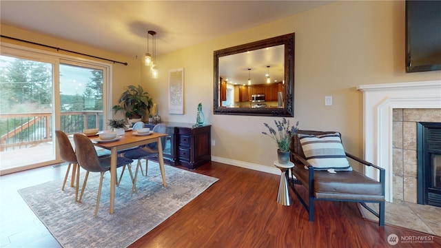 dining room featuring a tiled fireplace, baseboards, and wood finished floors