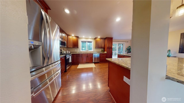 kitchen featuring light stone countertops, recessed lighting, appliances with stainless steel finishes, brown cabinetry, and dark wood-style flooring