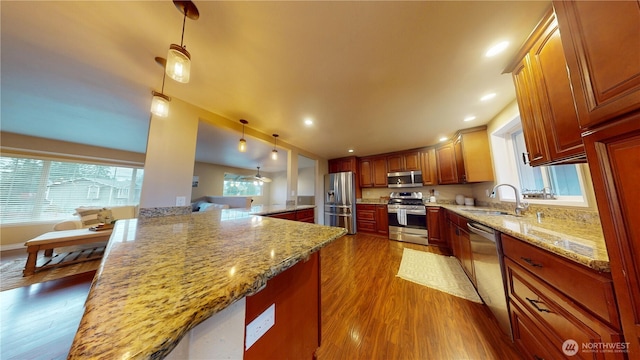 kitchen with a sink, decorative light fixtures, dark wood finished floors, stainless steel appliances, and light stone countertops