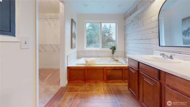 bathroom with vanity, a garden tub, a spacious closet, and wooden walls