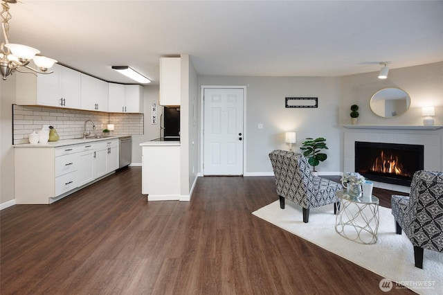 living area featuring dark wood finished floors, a notable chandelier, a tiled fireplace, and baseboards