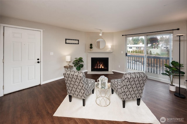 living area with baseboards, a lit fireplace, and wood finished floors